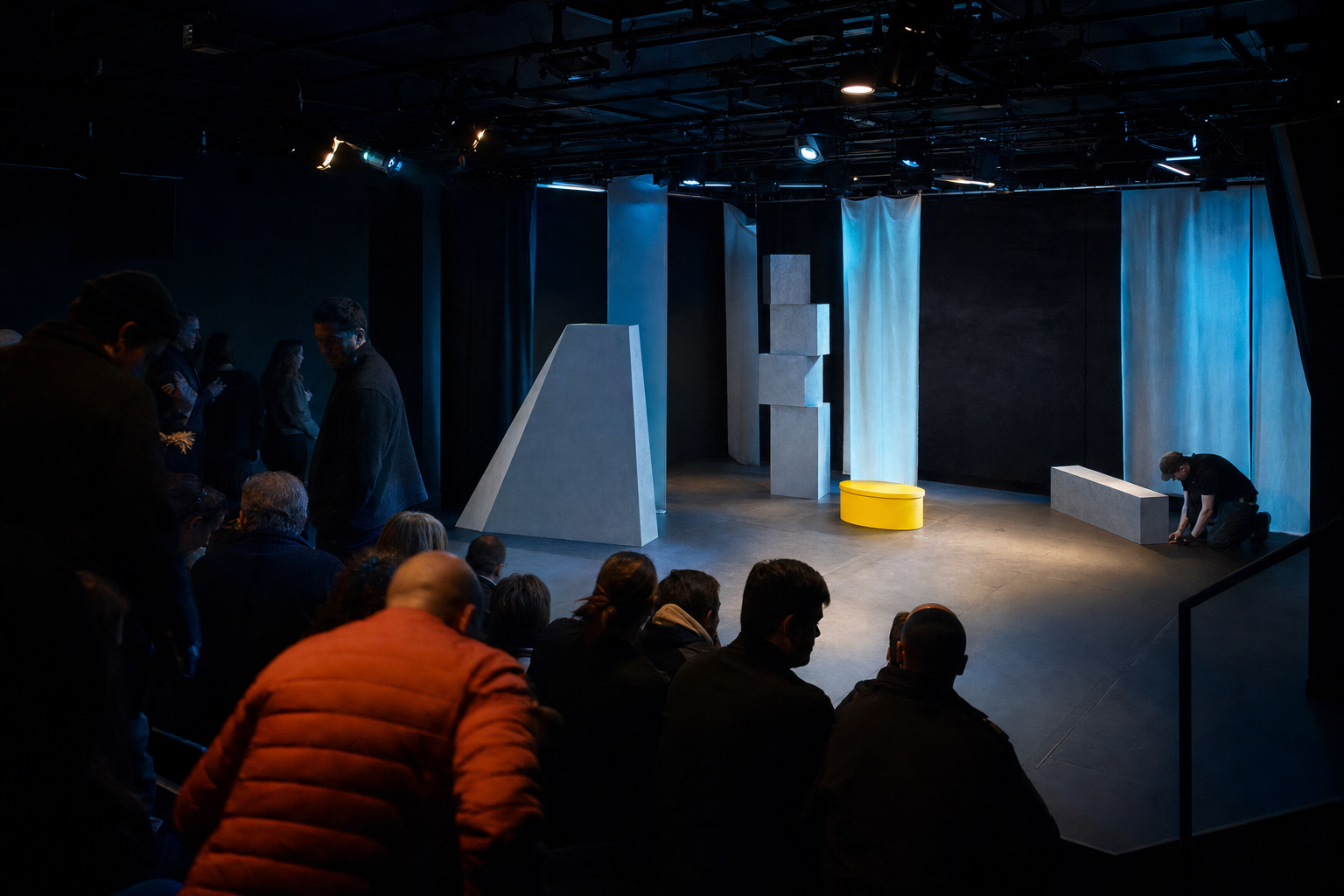 Publiek neemt plaats in een klein theater terwijl de laatste voorbereidingen op het podium plaatsvinden